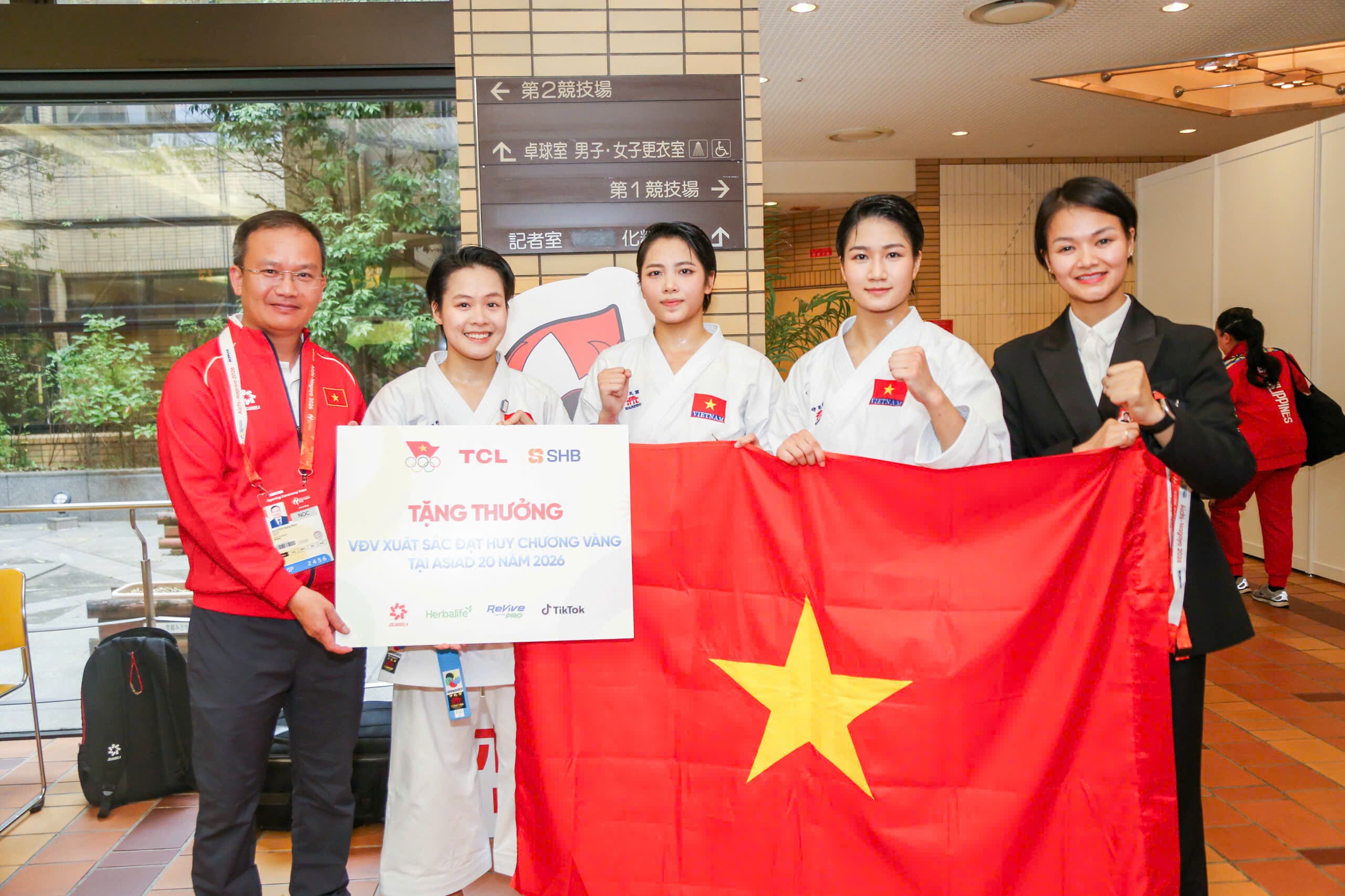 Đội tuyển karate đồng đội nữ nhận huy chương và phần thưởng từ lãnh đạo nhà tài trợ sau tấm HCV