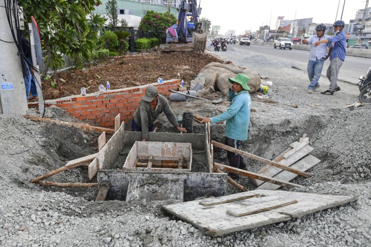 Hai bên đường, các công nhân tất bật thi công san lấp mặt đường, làm hệ thống cống.