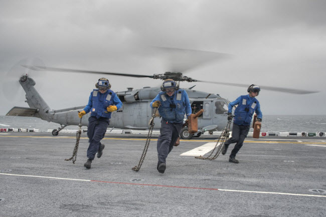 Các binh sĩ di chuyển tới nơi an toàn khi máy bay trực thăng SH-60 Sea Hawk cất cánh khỏi tàu sân bay USS Wasp.