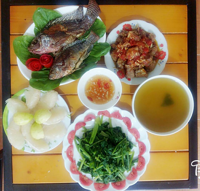 Mâm cơm có cá rô rán, thịt sốt cà chua, rau cải luộc và bưởi tráng miệng.
