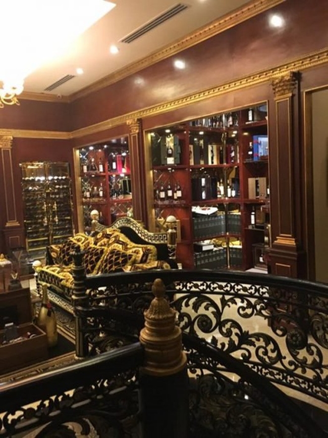 Cầu thang được chạm khắc tỉ mỉ kết hợp với bộ ghế salon cao cấp, hiện đại được đặt giữa phòng khách. Phía sau là các ngăn tủ trưng bày rượu đều được trang trí cầu kỳ.