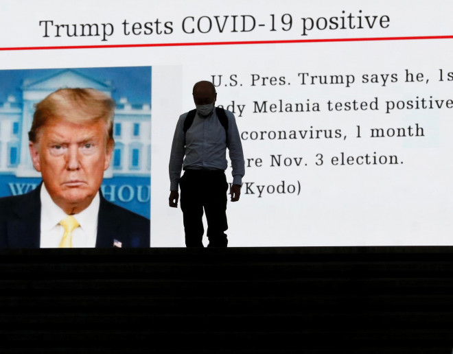 Một người dân Nhật Bản đi ngang màn hình ở Tokyo, phát tin Tổng thống Mỹ Donald Trump mắc Covid-19 Ảnh: REUTERS
