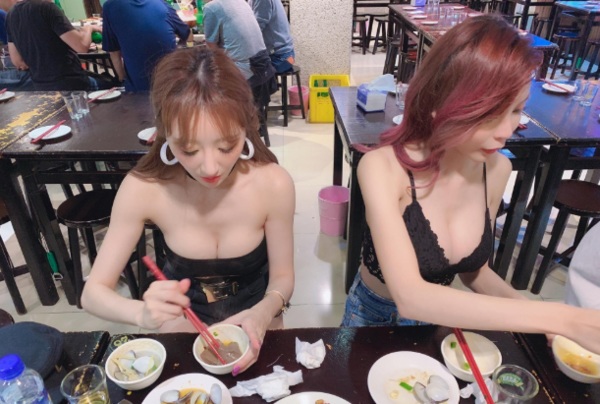 2 nữ PG hồn nhiên ăn uống với trang phục siêu ngắn, lộ vòng ngực nửa kín nửa hở.