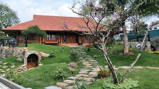 Căn nhà được xây hoàn toàn bằng gỗ tự nhiên, có hiên nhà để thư giãn, đường đi bằng đá xen giữa những thảm cỏ xanh non, cây cối, hoa cỏ xung quanh nhà.
