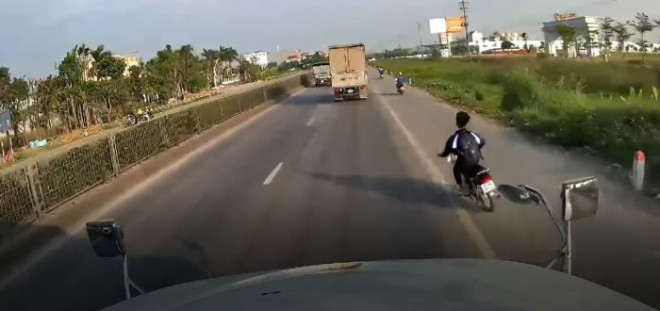 Hình ảnh nam thanh niên điều khiển xe máy điện, không đội mũ bảo hiểm, tạt đầu xe container