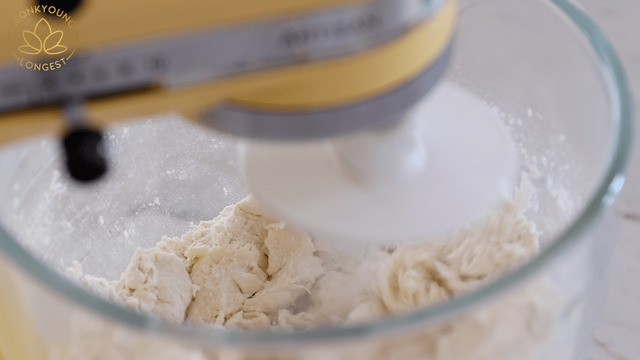 Cho bột mì, men nở và đường vào máy nhào bột, sau đó, đổ nước ấm vào máy và bật máy trộn ở tốc độ trung bình, nhào trong 3 – 4 phút cho đến khi thành một khối bột. Bạn cũng có thể nhào bột bằng tay.