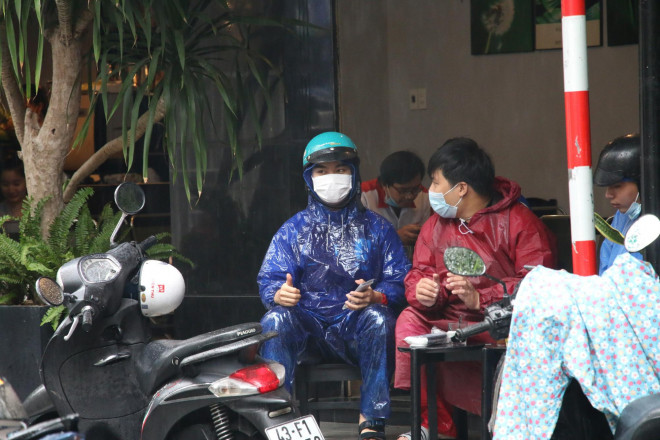 Người dân mang áo mưa uống cà phê tại đường Huỳnh Thúc Kháng