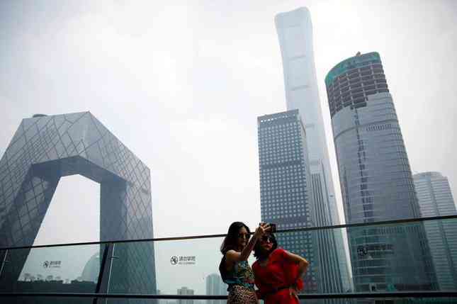Hai phụ nữ đứng chụp ảnh trước các toà nhà cao tầng ở Bắc Kinh, Trung Quốc. (Ảnh: Reuters)