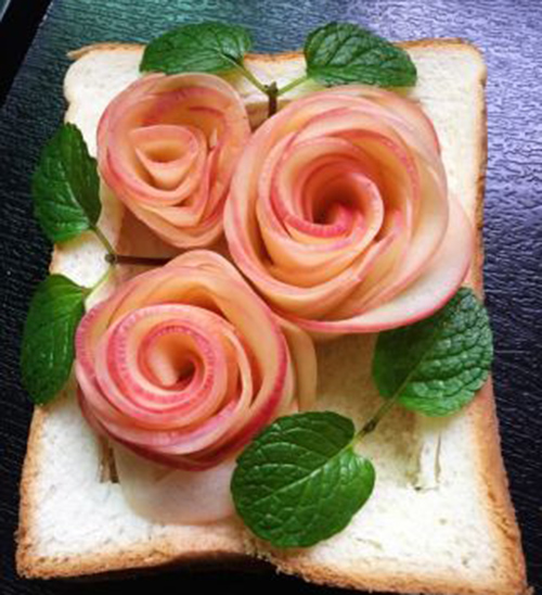  Các lát táo đã trải được cuộn từ mặt phải sang mặt trái, cuộn thành hình bông hồng rồi cho vào bánh mì như hình. Lần lượt làm hoa hồng thứ 2 và thứ 3, cuộn lại và đặt lần lượt vào.