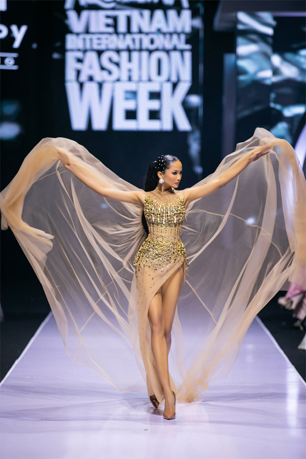 Mái tóc ngắn đặc trưng và làn da bánh mật từng là đặc điểm tạo nên sự khác biệt với mẫu số chung về cái đẹp của phụ nữ Việt Nam, H’Hen Niê luôn là một cái tên nhận được nhiều sự quan tâm và chú ý của giới mộ điệu Việt Nam chính vì lý do đó. Với NTK Thảo Nguyễn, H’Hen Niê là một người phụ nữ truyền cảm hứng về cái đẹp cùng với sự nỗ lực vượt bậc. Cô luôn “chọn mặt gửi vàng” những vị trí quan trọng cho Hoa hậu Hoàn vũ Việt Nam 2017. Trong show diễn lần này tại Tuần lễ Thời trang Quốc tế Việt Nam 2022, H'Hen Niê tiếp tục được “chọn mặt gửi vàng" cho vị trí vedette. Cô diện bộ đầm được đính hàng nghìn viên đá lấp lánh trên nền vải nude quyến rũ sexy, trong suốt, để lộ ra 3 vòng nóng bỏng mà vẫn tinh tế khéo léo của người con gái Ê Đê. Cùng với kiểu tóc đen dài, H’Hen Niê trông như một nữ hoàng, xinh đẹp và đầy kiêu hãnh trên sàn diễn.
