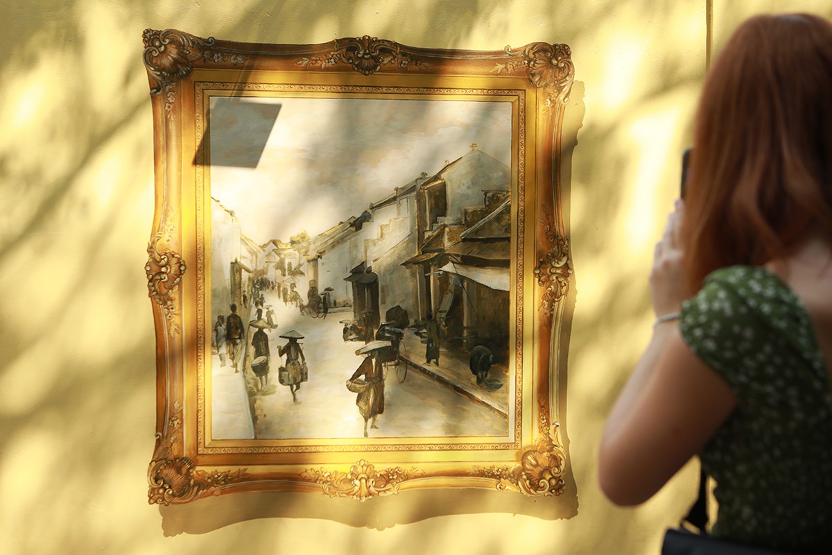 Một du khách nước ngoài thích thú đi một vòng ngắm từng bức tranh và chụp lại làm kỉ niệm