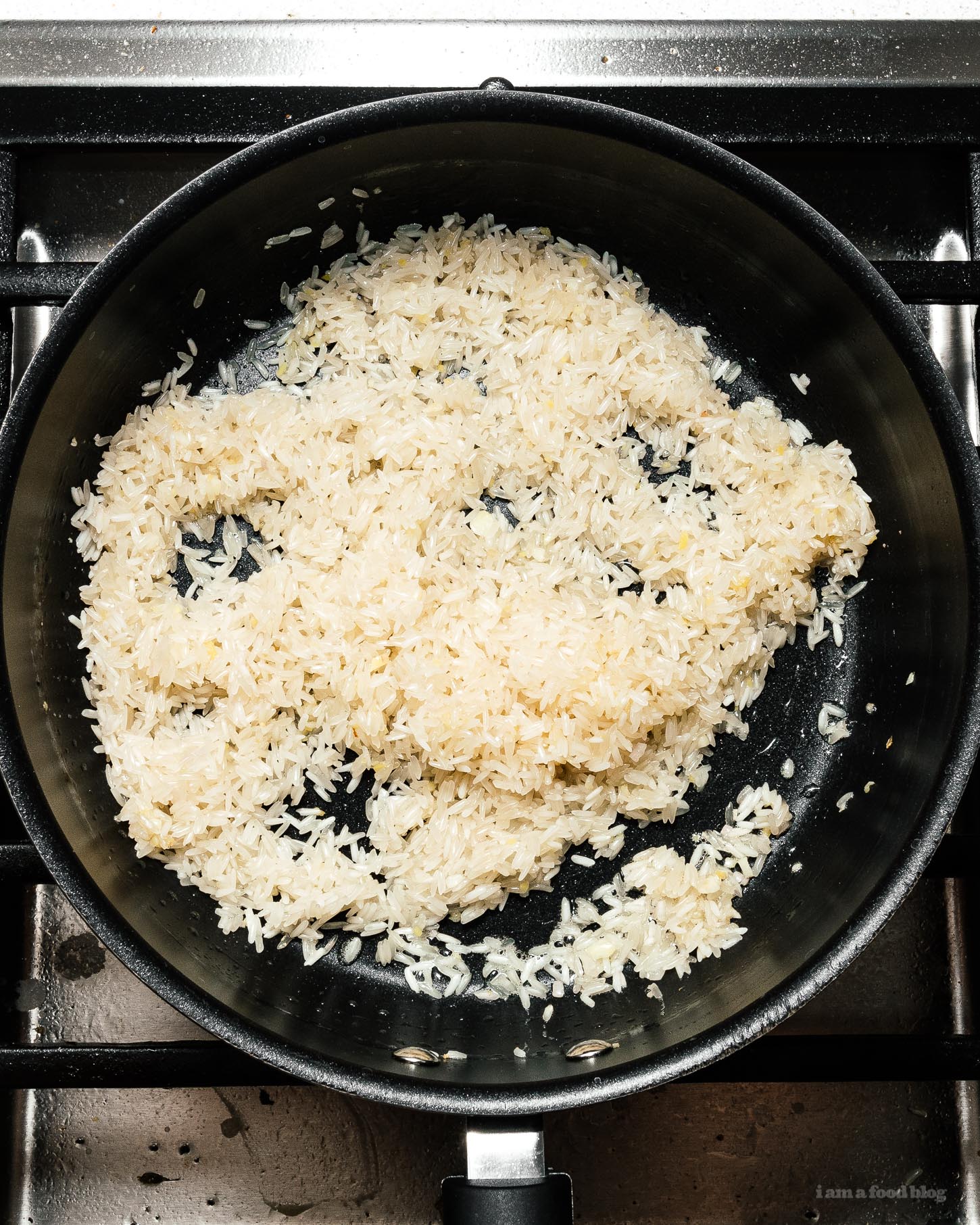 Trong chảo hoặc nồi có nắp, đun nóng mỡ gà.&nbsp;Thêm gừng, tỏi và hẹ, khuấy đều cho dậy mùi thơm rồi trút gạo vào rang đến khi thấy từng hạt gạo bóng.