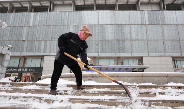 Một công nhân xúc tuyết trước trung tâm mua sắm ở Bắc Kinh - Trung Quốc hôm 14-12. Ảnh: Reuters