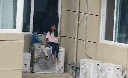 Hai đứa trẻ ngồi trên cục nóng điều hòa.