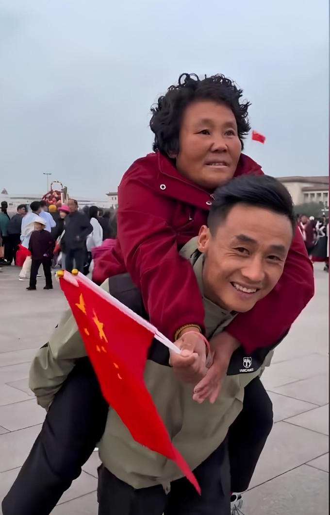 Tiểu Cương cõng mẹ xem thượng cờ ở Thiên An Môn hôm 17/10. Ảnh: Dazhong Daily