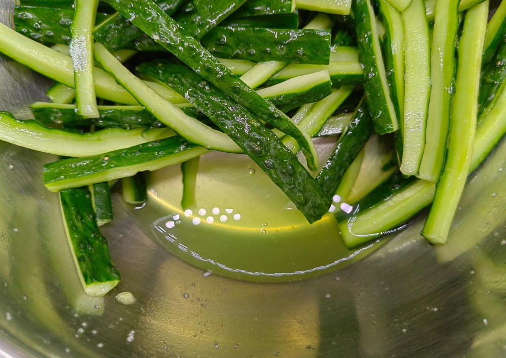 Cho dưa chuột vào đĩa lớn, rắc 10g muối ăn lên, sau đó trộn đều, ướp trong 30 phút. Dưa chuột sau khi ướp sẽ tiết ra nhiều nước, vì vậy chúng ta cần rửa sạch dưa chuột bằng nước để loại bỏ muối thừa, sau đó vắt khô nước và để sang một bên.