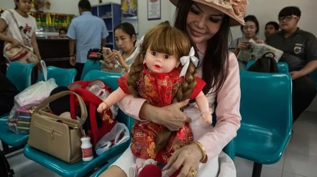 Một phụ nữ đợi ở bến xe bus tại Nakhon Sawan, Thái Lan cùng búp bê Kumanthong của mình. Ảnh: Usatoday