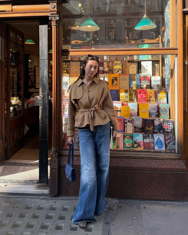 Phong cách Parisian Chic được hoa hậu thể hiện qua bộ cánh gồm măng tô dáng ngắn, quần jeans và giày lưới Alaia. Chiếc túi Hermes Constance giá hơn 300 triệu đồng hoàn thiện set đồ màu trung tính.