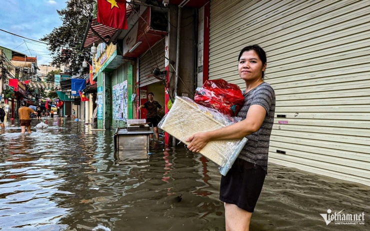 Chị Chi lội nước bê đồ đi di tản. Ảnh: Huy Nguyễn