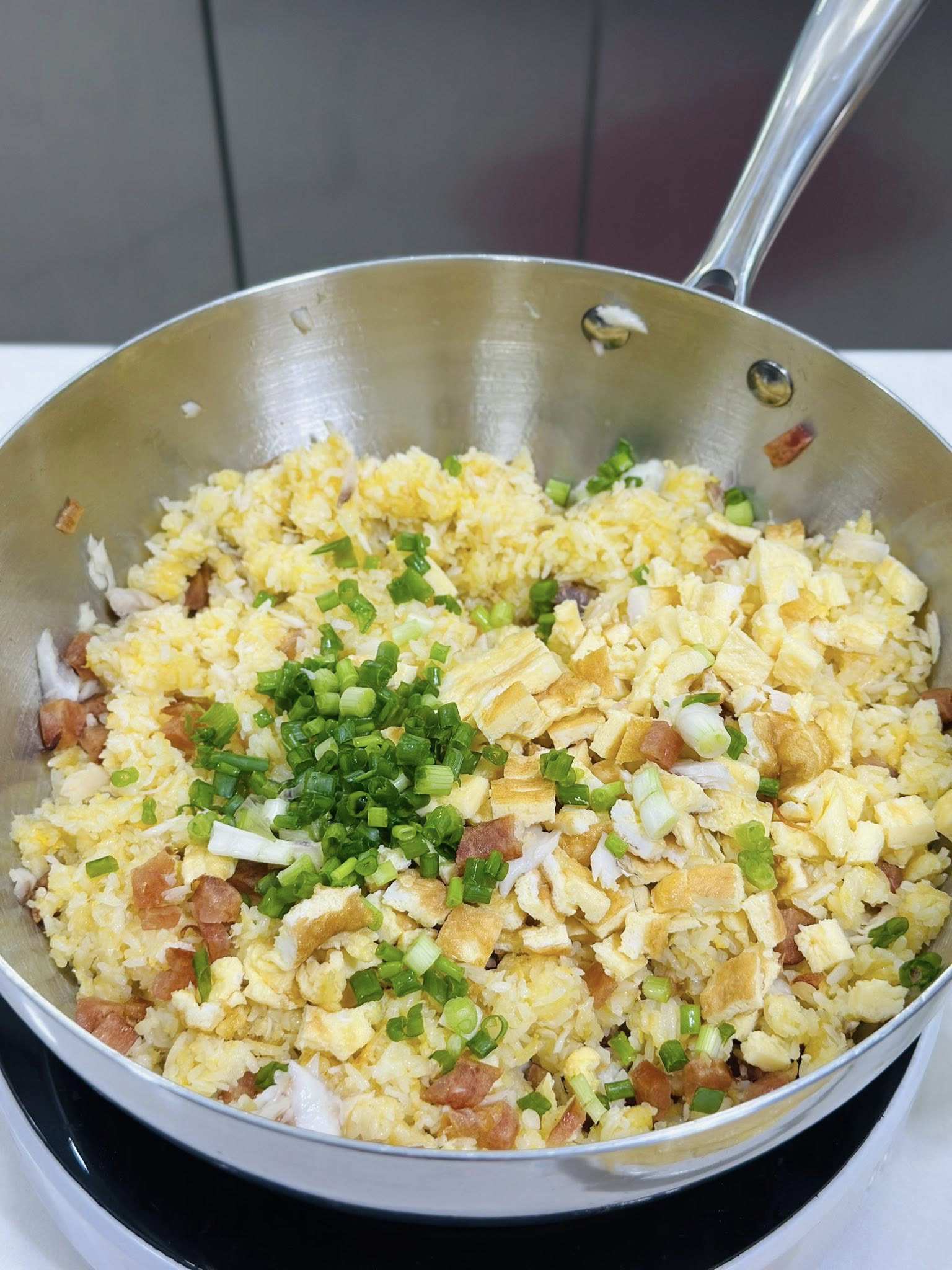 Cho cơm vào rang đến khi hạt săn, tơi đều, rồi trộn cá và&nbsp;lạp xưởng vào. Khi cơm gần chín thì cho trứng đã cắt hạt lựu và hành lá vào đảo đều, tắt bếp.