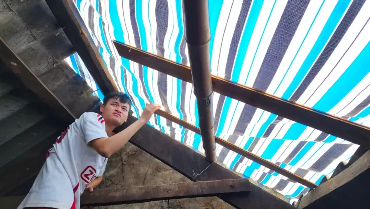 Con trai ông Đạt chằng chéo lại tấm bạt tạm để nước mưa không chảy vào nhà. Ảnh: MINH TRƯỜNG.