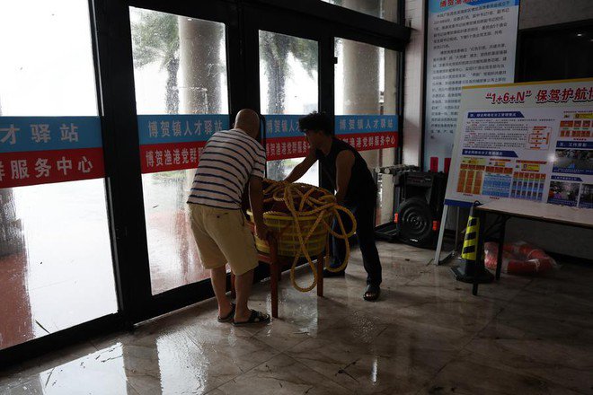 Sóng lớn ập vào cảng biển trong khi người dân phải cố chặn cửa để chống lại gió mạnh vào hôm 5-10 ở TP Mậu Danh, tỉnh Quảng Đông - Ảnh: TÂN HOA XÃ