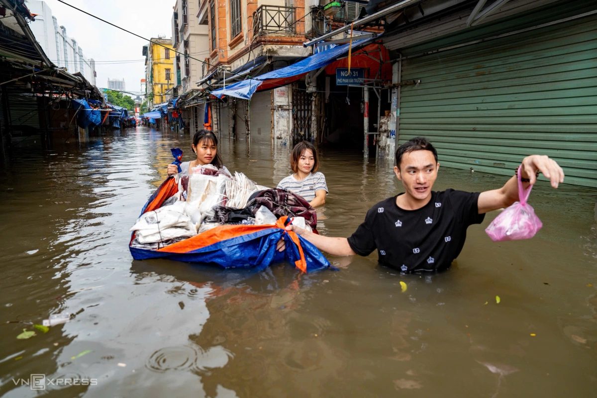 Nhóm tiểu thương dùng bạt làm "thuyền" vận chuyển hàng hóa trong nước ngập. Ảnh: Tùng Đinh
