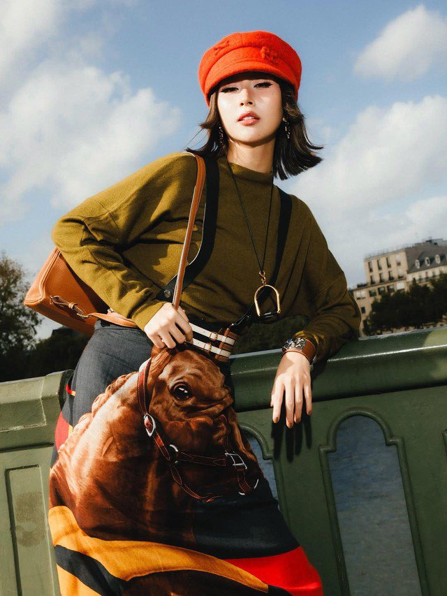 Trong loạt ảnh mới tại Paris, Quỳnh Anh Shyn diện áo dài tay tông xanh olive - gam màu mang hơi hướng cổ điển nhưng được làm mới nhờ cách phối cùng chân váy lụa biến tấu từ khăn in hình ngựa.