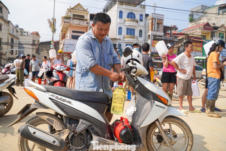Ông Khải mua xăng, bên cạnh là chiếc máy bơm đặt dưới gầm xe, chuẩn bị mang về để hút nước trong nhà.