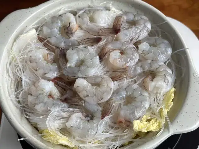 Tôm tươi bóc vỏ, bỏ đầu nhưng giữ lại phần đuôi. Dùng dao rạch nhẹ lưng tôm để lấy chỉ đen. Khi mở lưng tôm như vậy, gia vị sẽ dễ thấm hơn. Xếp tôm thành vòng tròn lên miến, đuôi hướng lên trên cho đẹp mắt.