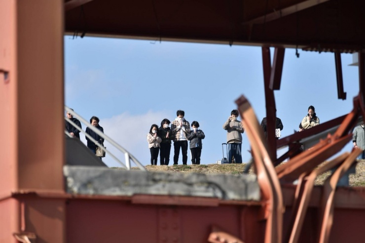 Mọi người dành một phút mặc niệm vào ngày 11-3-2025 gần tàn tích của trung tâm phòng chống thiên tai cũ ở Minamisanriku, tỉnh Miyagi. Ảnh: The Japan Times