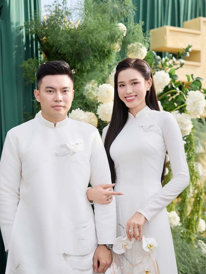 Vợ chồng Đỗ Thị Hà diện áo trắng thêu họa tiết cánh chim. Hoa hậu cầm vòng hoa lan thay cho bó hoa cưới thông thường