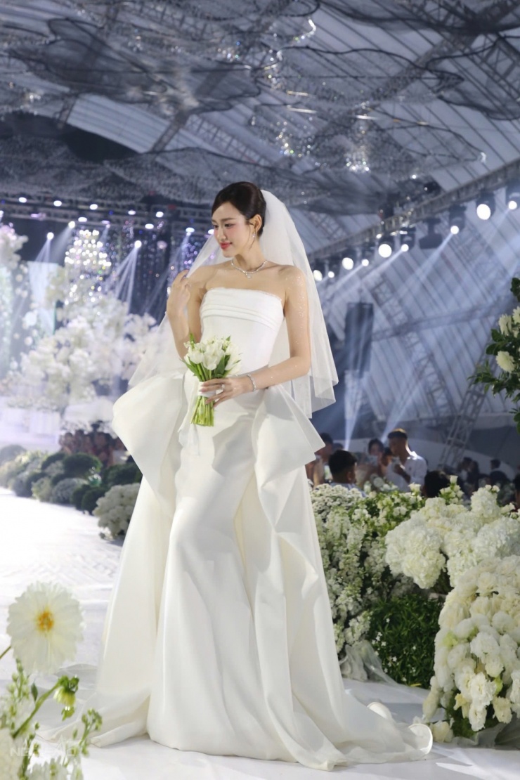 Khoảng 17h, Đỗ Thị Hà diện chiếc váy cưới xòe bồng, có mặt tại khu tổ chức hôn lễ ở khu đô thị Nam Cầu Dài, phường Đồng Hới, để đón khách dự tiệc. Trang phục giúp cô khoe vai trần mảnh mai, vẻ ngoài ngọt ngào tựa công chúa.