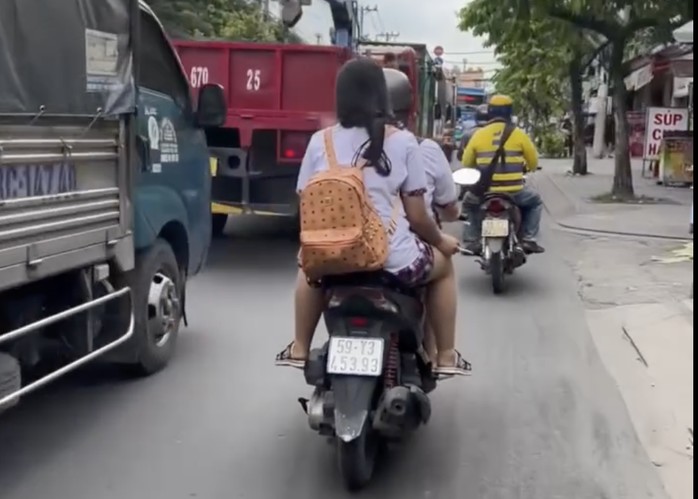 Nữ sinh phía sau không đội mũ bảo hiểm, phì phèo điếu thuốc.