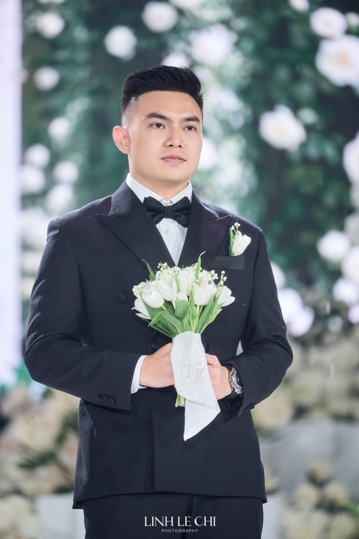 Chú rể Nguyễn Viết Vương cầm bó hoa tulip, cài chiếc khăn thêu lồng hai chữ cái đầu trong tên của cô dâu chú rể: V và H. Anh hồi hộp chờ bà xã tiến gần.