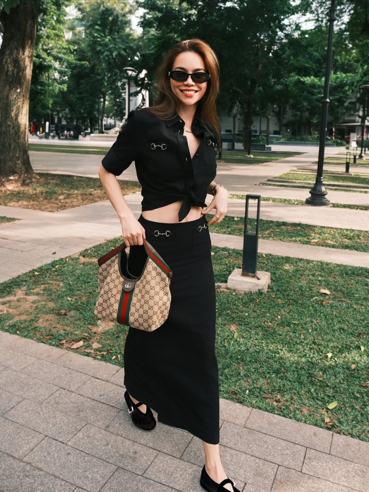 Bà mẹ ba con dạo chơi trên phố Hà Nội với cả bộ màu đen, gồm sơ mi và chân váy midi dáng cột, phối giày búp bê da lộn. Để trang phục bớt đơn điệu, cô tạo điểm nhấn bằng túi Gucci màu nâu in họa tiết monogram đặc trưng của nhà mốt Italy.