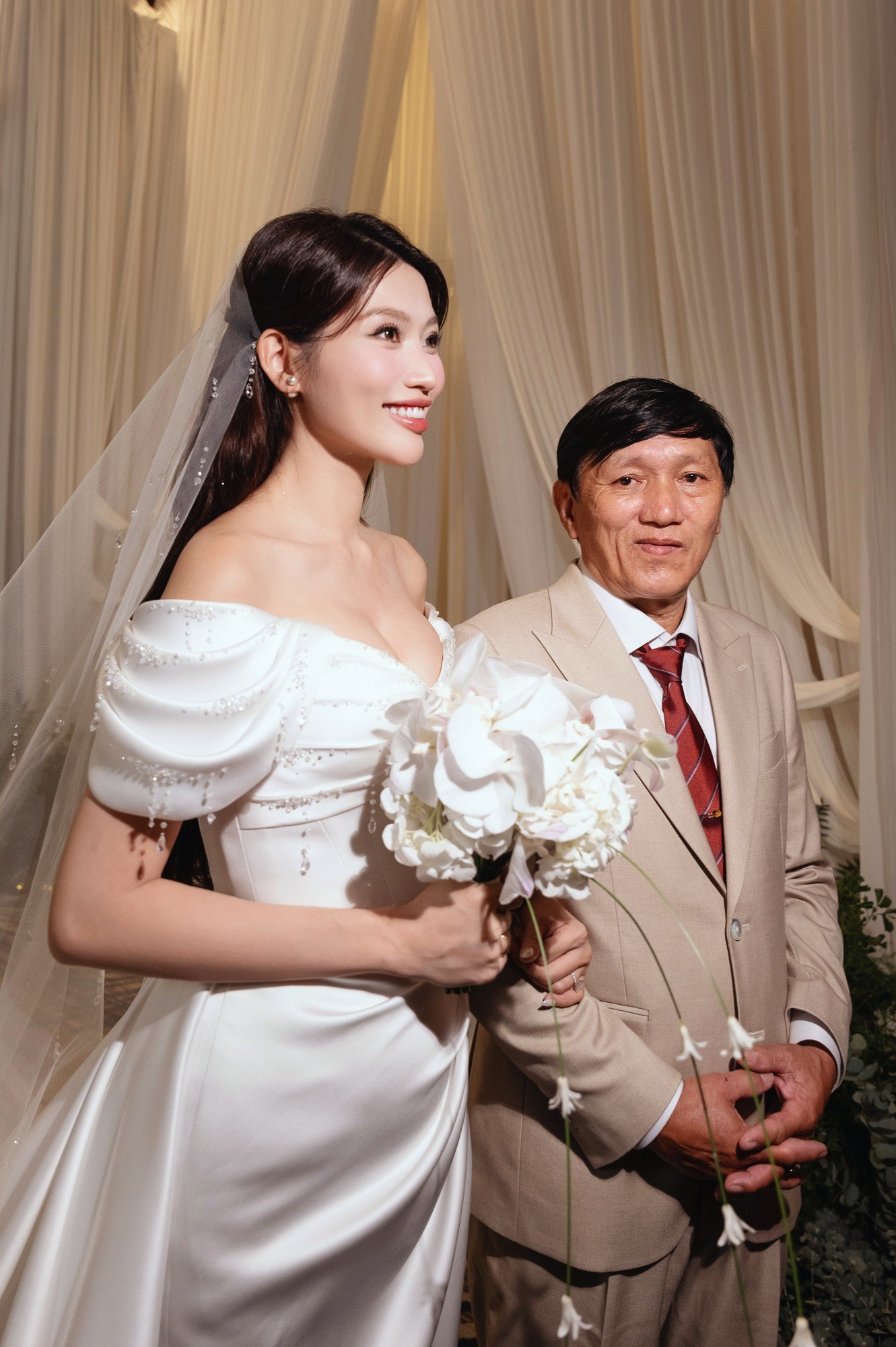 Khoảnh khắc Quỳnh Châu được cha dẫn lên sân khấu khiến nhiều khách mời xúc động. Cha mẹ hai bên gửi lời chúc phúc và dặn dò con trong không khí ấm cúng. Hôm nay cũng là dịp kỷ niệm 50 năm ngày cưới của cha mẹ chú rể. Doanh nhân Phát Nguyễn không giấu được xúc động khi nhìn thấy vợ bước lên sân khấu.
