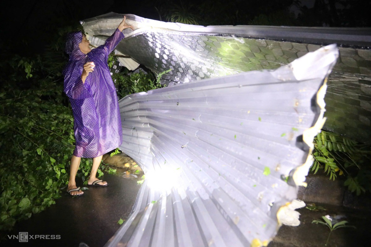 Ông Hòa mặc áo mưa, rọi đèn thu dọn lại khu vực trước nhà sau khi sức gió giảm. Ảnh: Đình Văn