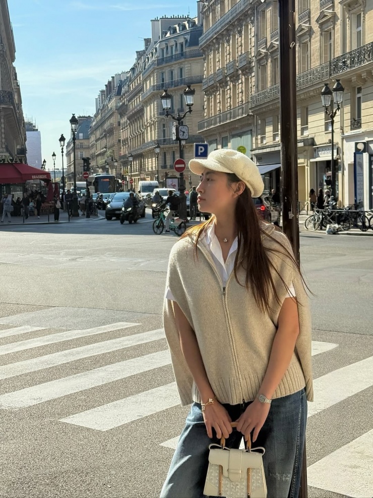 Hoa hậu Lương Thùy Linh tạo sự khác biệt bằng mẫu áo len dáng cape màu be, kết hợp sơ mi cộc tay, quần jeans dáng rộng và túi Goyard. Cô tạo điểm nhấn cổ điển bằng mũ beret vải tweed.