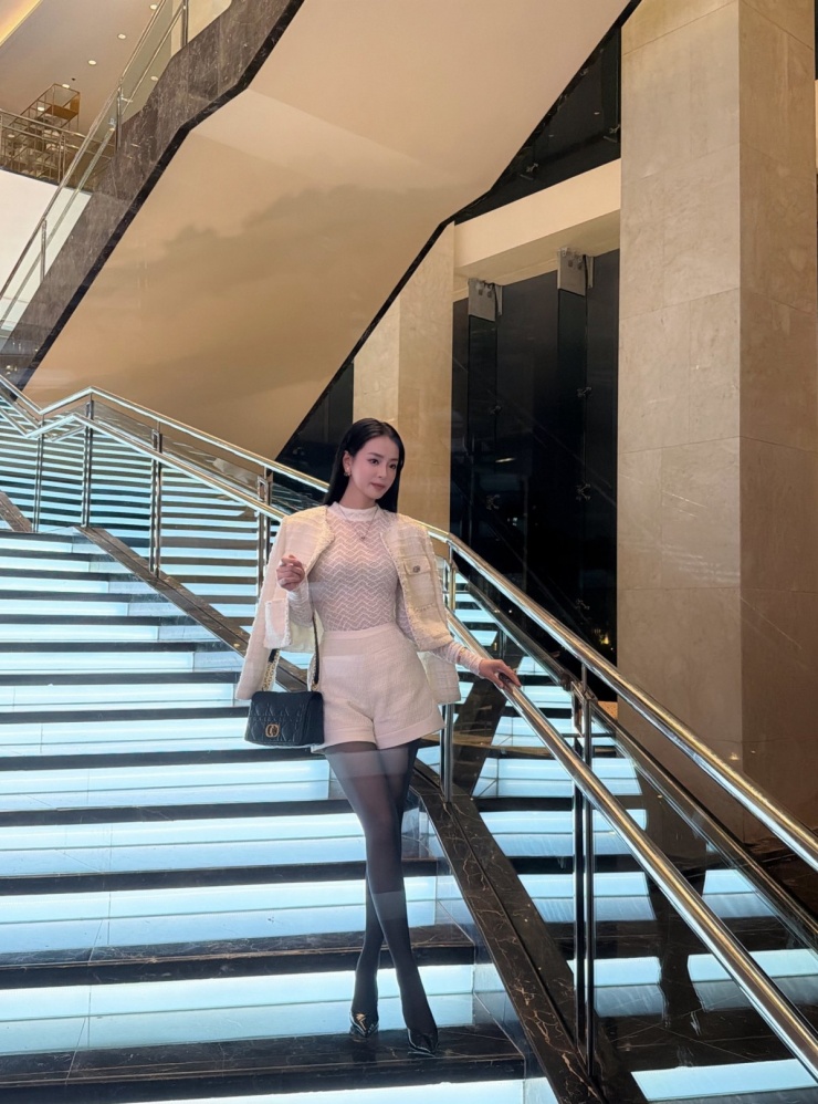 Á hậu Bùi Khánh Linh diện set đồ tweed hồng nhạt phối áo lưới ôm dáng, tạo vẻ nữ tính, quyến rũ. Cô xách túi Dior Caro Bag màu đen, được nhà mốt bán với giá khoảng 135 triệu đồng.