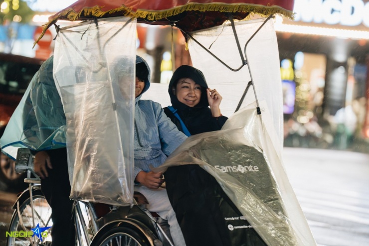 Du khách nép mình tránh bị mưa tạt khi dạo phố đêm Hà Nội. Trời rét và mưa khiến lượng khách đi xích lô giảm, đường phố vắng hơn thường ngày.