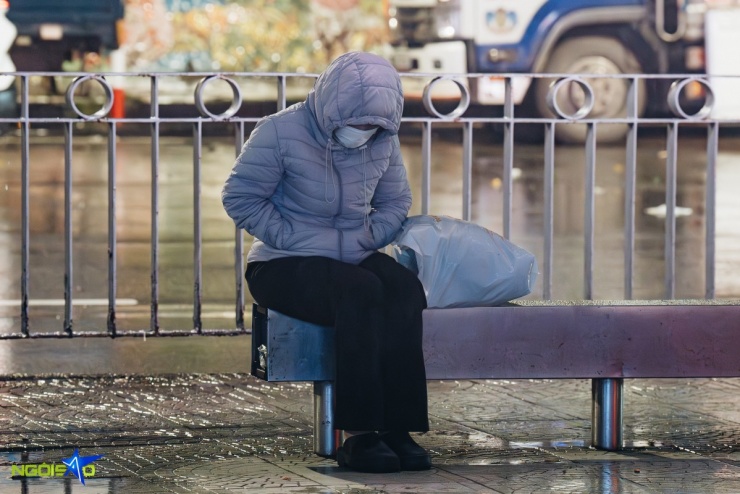 Người phụ nữ ngồi rung chân để làm ấm cơ thể trong lúc chờ xe buýt tại điểm trung chuyển Long Biên.