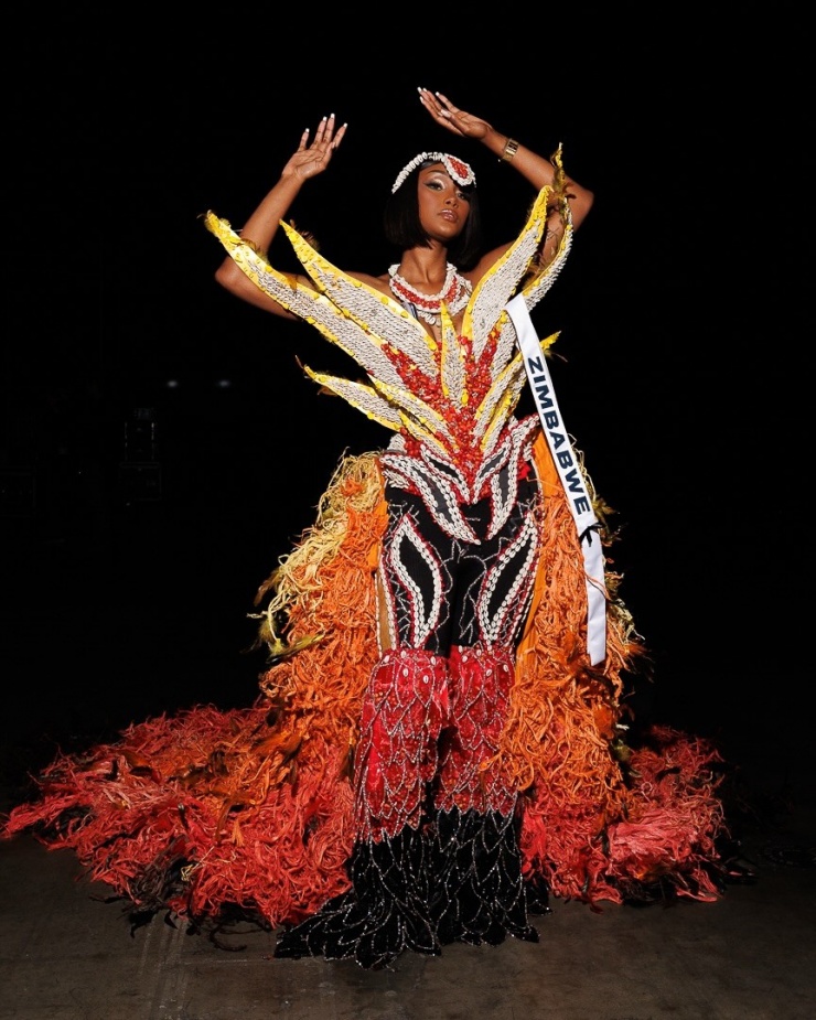 Thí sinh Zimbabwe Lyshanda Moyas diện trang phục mang sắc đỏ, vàng và đen, gợi hình ảnh ngọn lửa bùng lên từ mặt đất. Thiết kế được tạo nên từ các dải vải sợi dài, đính kết thủ công. Trang phục điểm thêm chuỗi hạt và các họa tiết truyền thống, nhấn mạnh bản sắc văn hóa quốc gia.