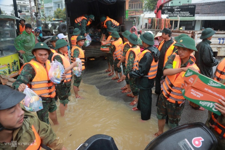 Mì gói, bánh ngọt, nước uống được bộ đội chuyền tay từ trên thùng xe xuống thuyền thúng, cano để tiếp tế người dân vùng ngập.
