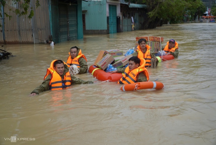 Một nhóm cảnh sát mặc áo phao, chất mì gói lên các phao nổi, cột dây cố định kéo vào vùng ngập chia cho từng hộ dân.
