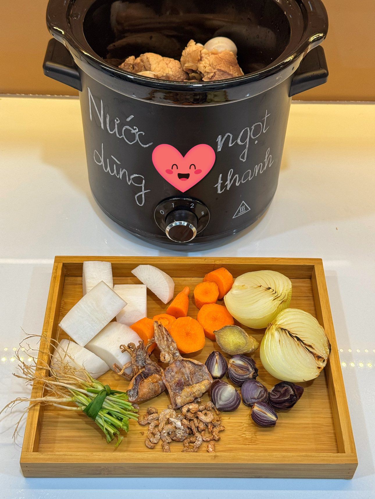 Cho xương xuống đáy nồi, xếp củ cải, cà rốt, gừng, rễ rau mùi, mực khô, tôm khô, hành tây, hành tím lên trên.