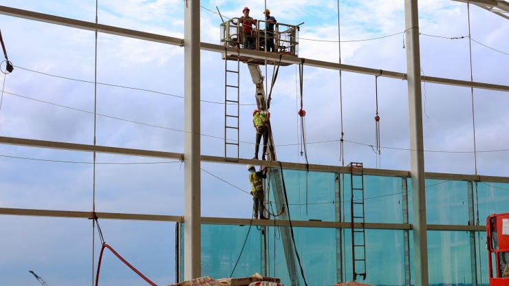 Từng nhóm công nhân được xe cẩu nâng lên để hoàn thiện phần kính. Mỗi tấm kính nặng khoảng 350-900 kg.