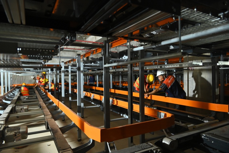 Hệ thống thang bộ, thang máy, băng tải và băng chuyền đang được lắp đặt giữa các tầng nhà ga, yêu cầu độ chính xác cao theo tiêu chuẩn hàng không. Bên trong, hàng trăm công nhân thi công liên tục. Toàn dự án huy động gần 14.000 kỹ sư, chuyên gia, công nhân và hơn 3.000 thiết bị.