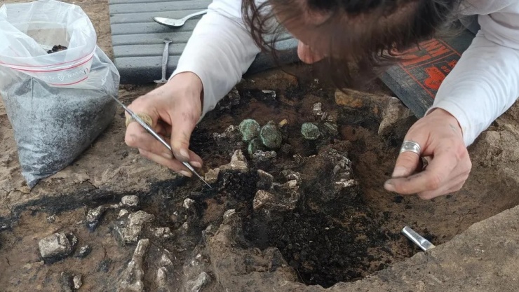 Nhà khảo cổ học đang lấy ra kho tiền xu được tìm thấy trong ngôi mộ thời La Mã. Những đồng tiền xu này có thể đã được cất giữ trong một chiếc ví. (Nguồn ảnh: Frédéric Prodeo/INRAP)