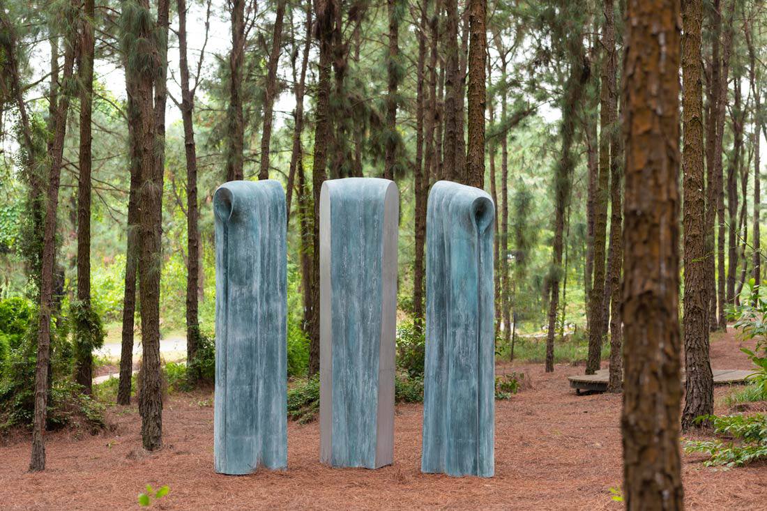 Tác phẩm “Nguồn” của nhà điêu khắc Hoàng Mai Thiệp. Từ nhiều năm nay, Hoàng Mai Thiệp theo đuổi mạch sáng tác về cội rễ. Nguồn là lát cắt của Thiên - Địa - Nhân, là nơi mọi dòng chảy bắt đầu. Tác phẩm hòa vào khu rừng như một ký ức khởi nguyên, nhắc con người tìm lại căn cốt của mình.